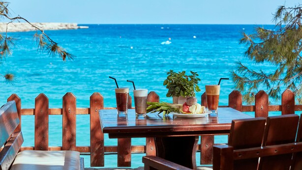A wooden table with drinks and a plate of food, overlooking a turquoise sea. - Grecian Park Hotel (Paralimni)
