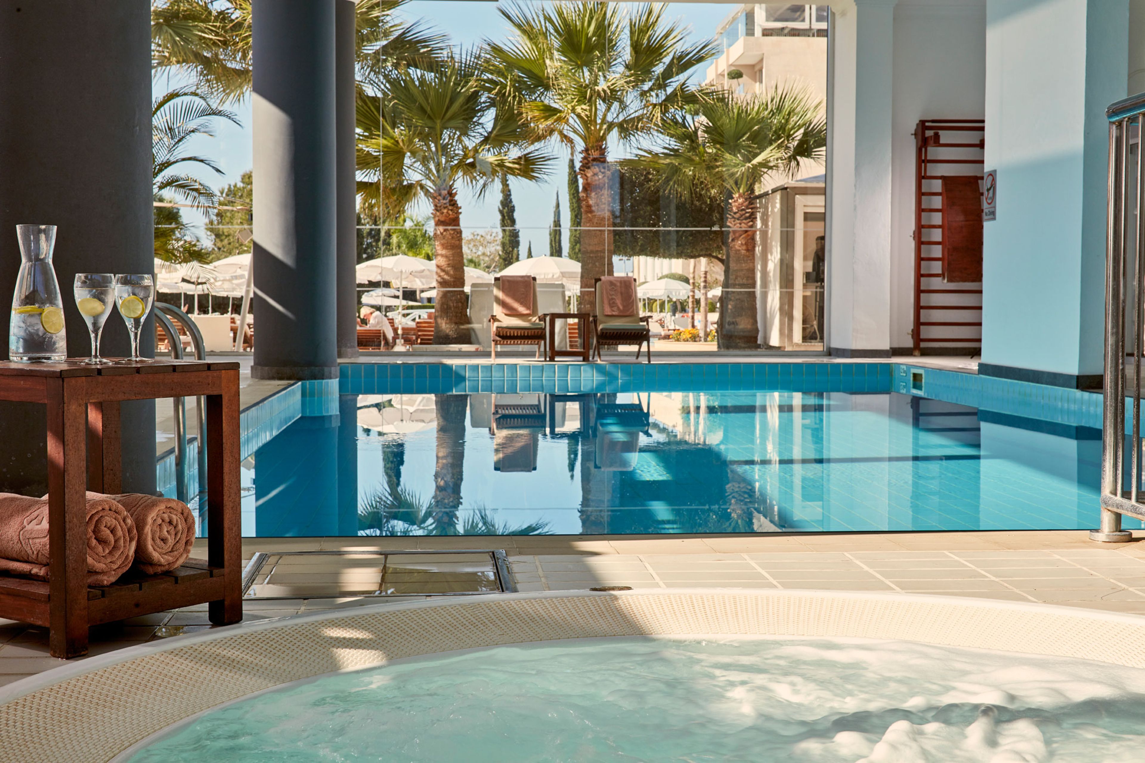 Zona de piscina con sillas de descanso, jacuzzi y mesa con toallas y vasos.