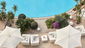 A rooftop pool area with white umbrellas, lounge chairs, and a variety of plants.
