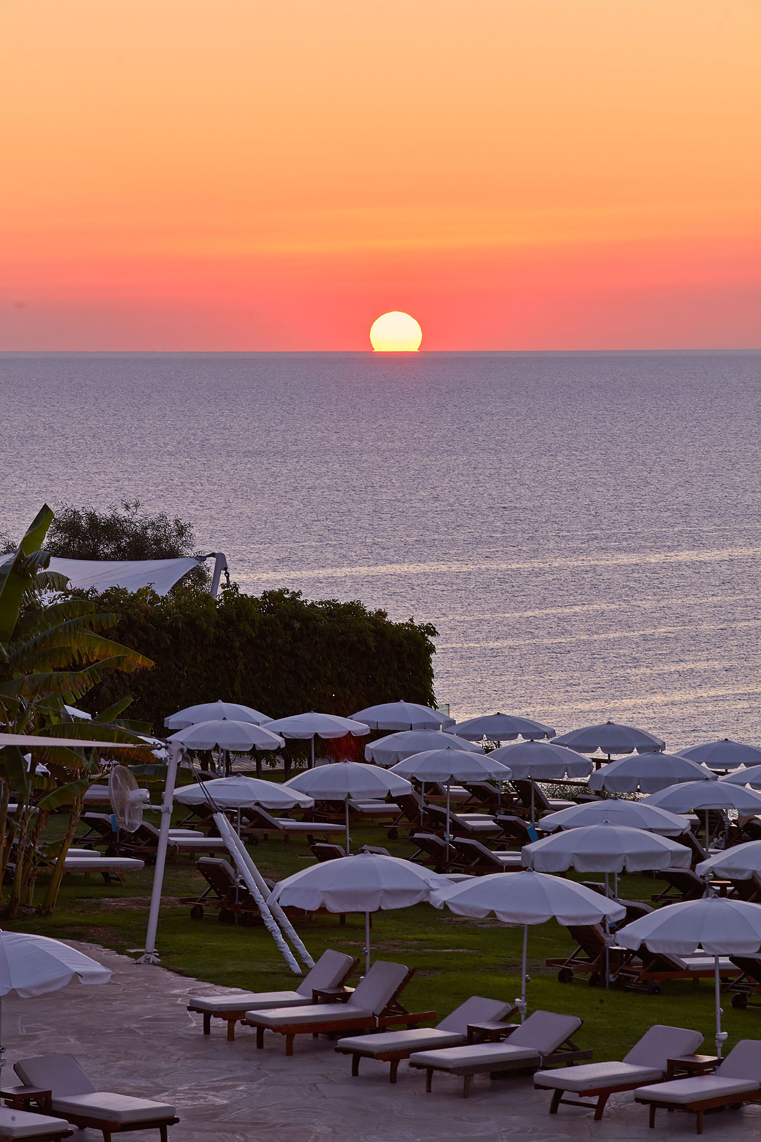 A sunset view over the ocean with lounge chairs and umbrellas.