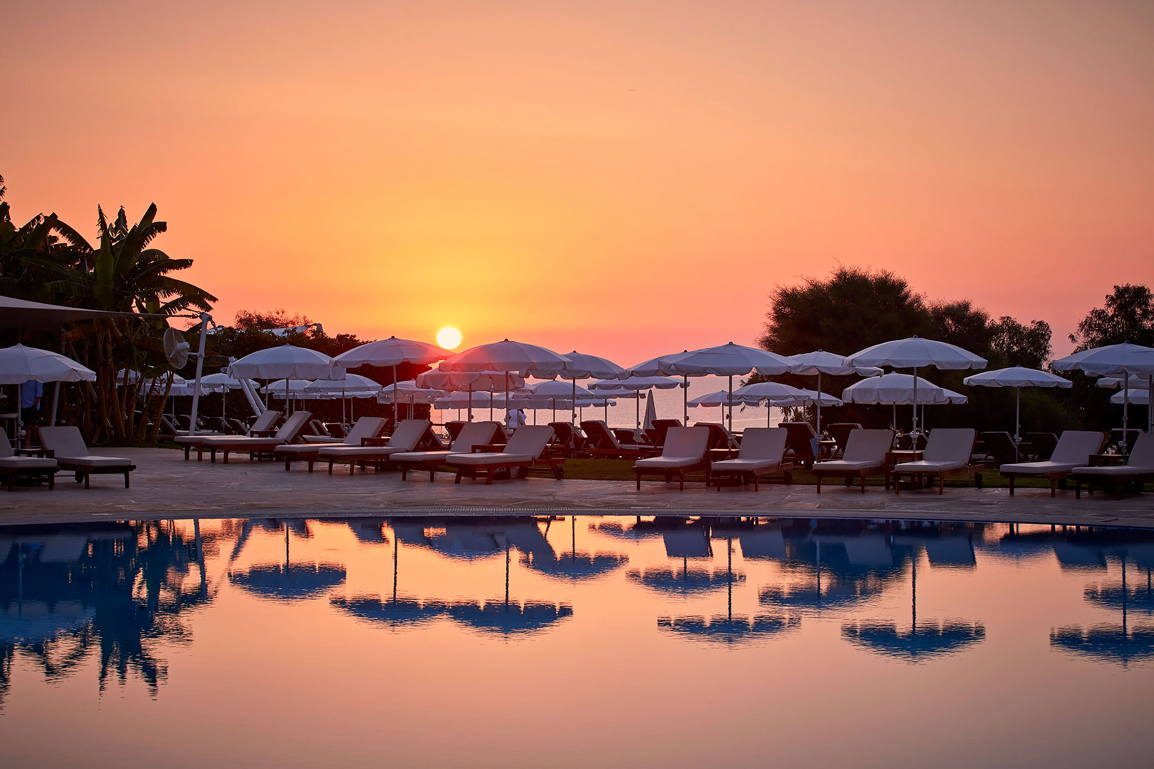 Un área junto a la piscina con sillas de descanso y sombrillas durante el atardecer.