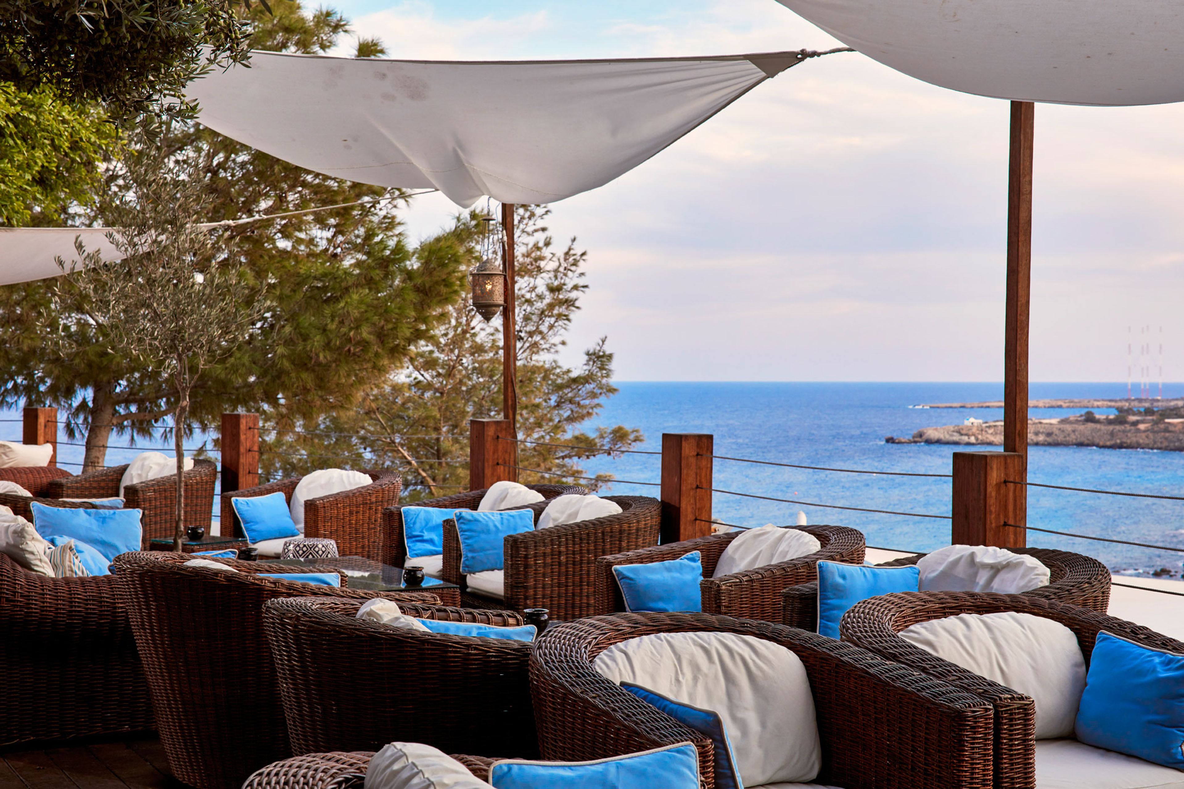 Wicker furniture with cushions, a view of the sea, and a wooden structure.