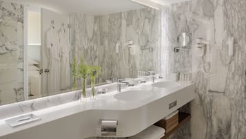 A modern bathroom with a large marble vanity, two sinks, a mirror, and a shower area.
