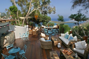 Un patio al aire libre con mobiliario de mimbre, mesas y sillas, con vistas panorámicas.
