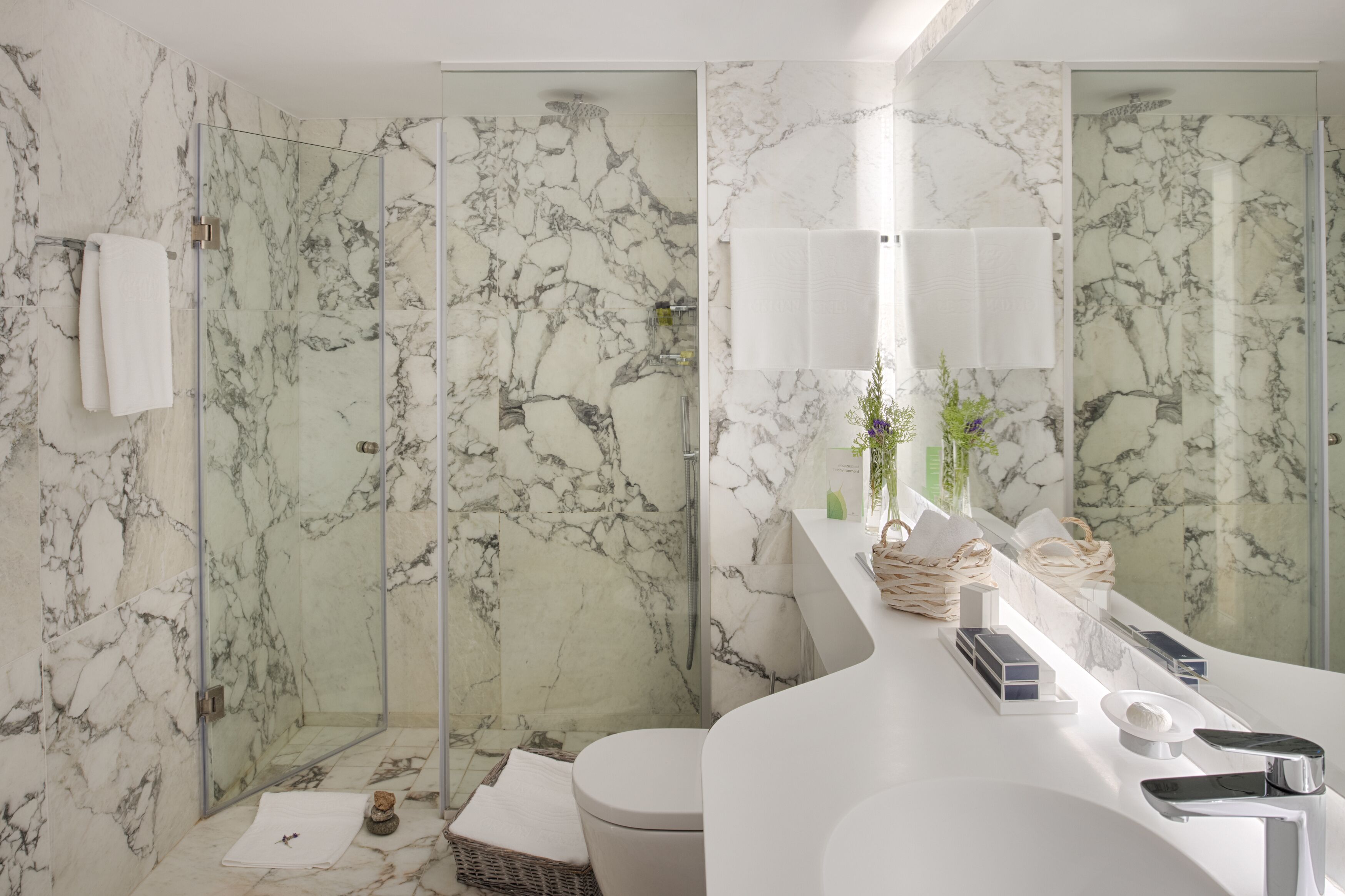 A modern bathroom with marble walls, a glass shower enclosure, a white sink with a mirror, and a toilet.