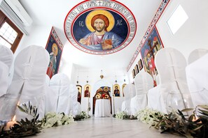 En kyrkas interiör med vita stolar, ett altare i mitten och religiösa målningar på väggarna.