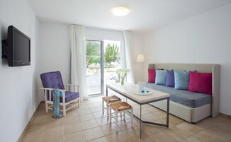 Una habitación de hotel moderna con sofá, una silla, una mesita y televisor montado en la pared.