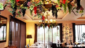 A dining area with a chandelier made of grapevines and leaves, wooden furniture, and a view of the outdoors through large windows. - Aliathon Aegean (Geroskipou)
