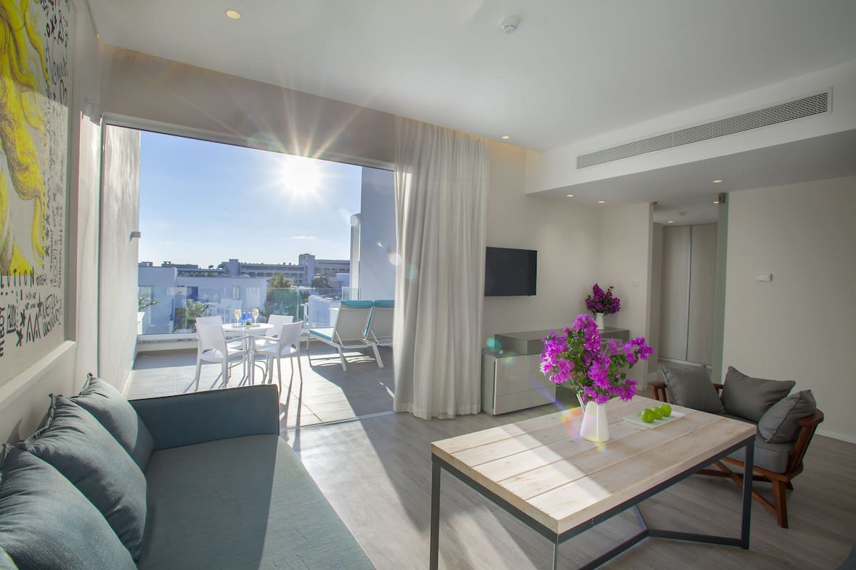 Una sala de estar moderna con un sofá, una mesa de centro y un televisor. Hay un balcón con vistas a la ciudad.