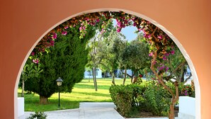 An arched pathway leading to a garden with a tree and a lamppost. - Aliathon Aegean (Geroskipou)