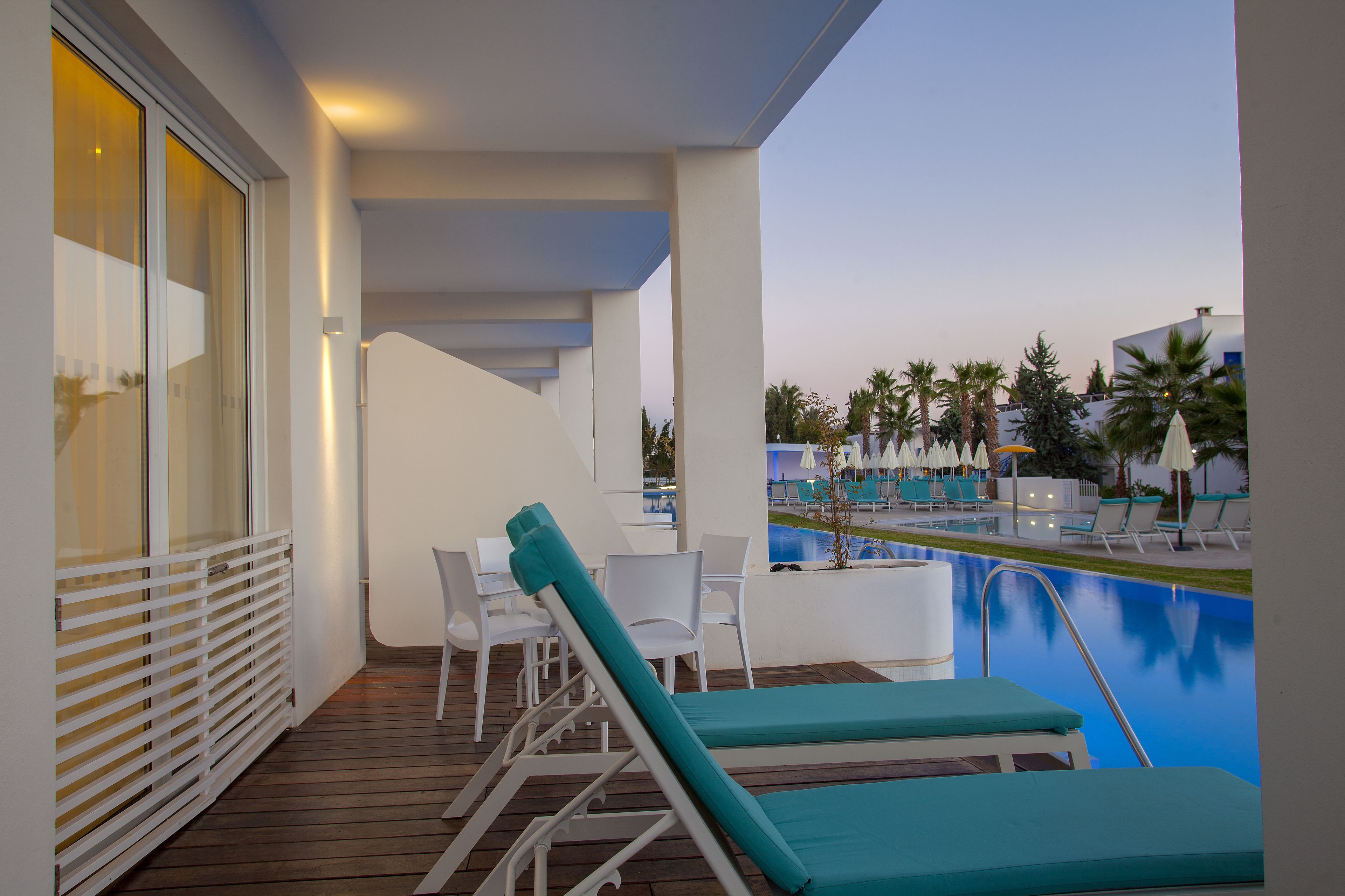 Zona junto a la piscina con sillones reclinables y una mesa, con vistas a una piscina y palmeras.