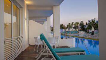Zona junto a la piscina con sillones reclinables y una mesa, con vistas a una piscina y palmeras.