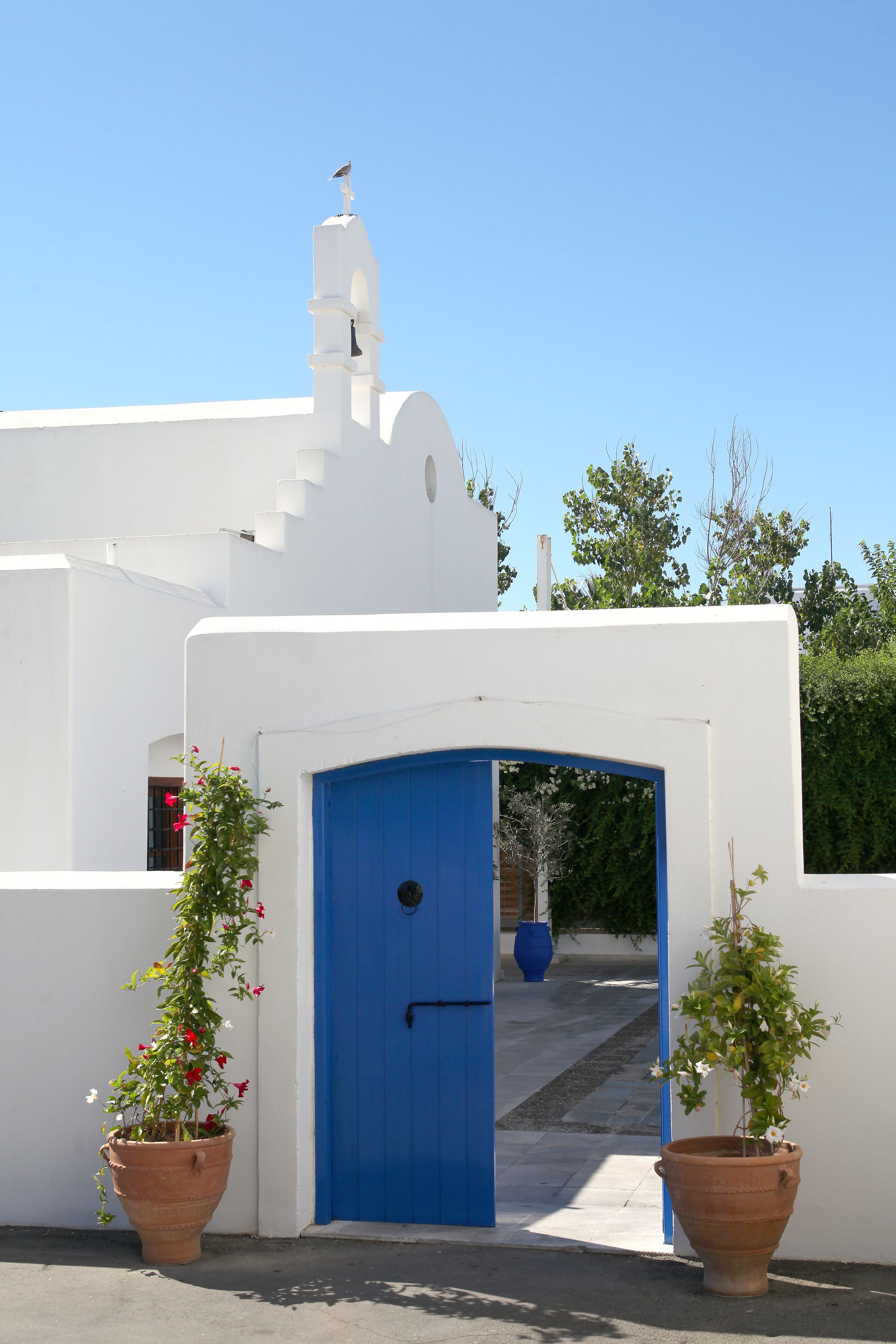 Un edificio blanco con una puerta azul y dos macetas de terracota con plantas.