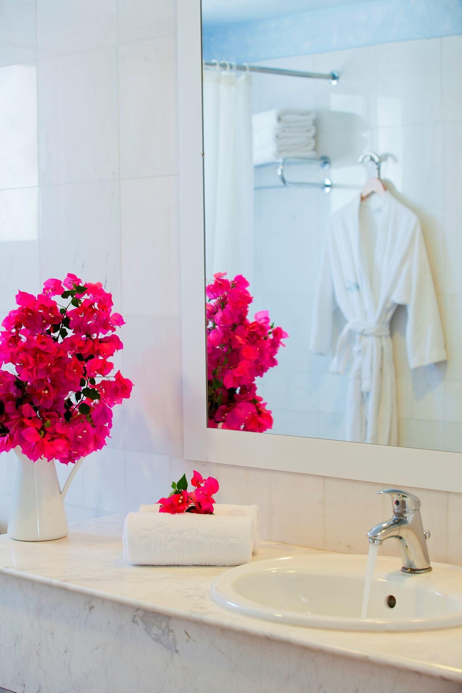 Une salle de bain avec un lavabo blanc, un miroir et des fleurs roses posées sur le comptoir.