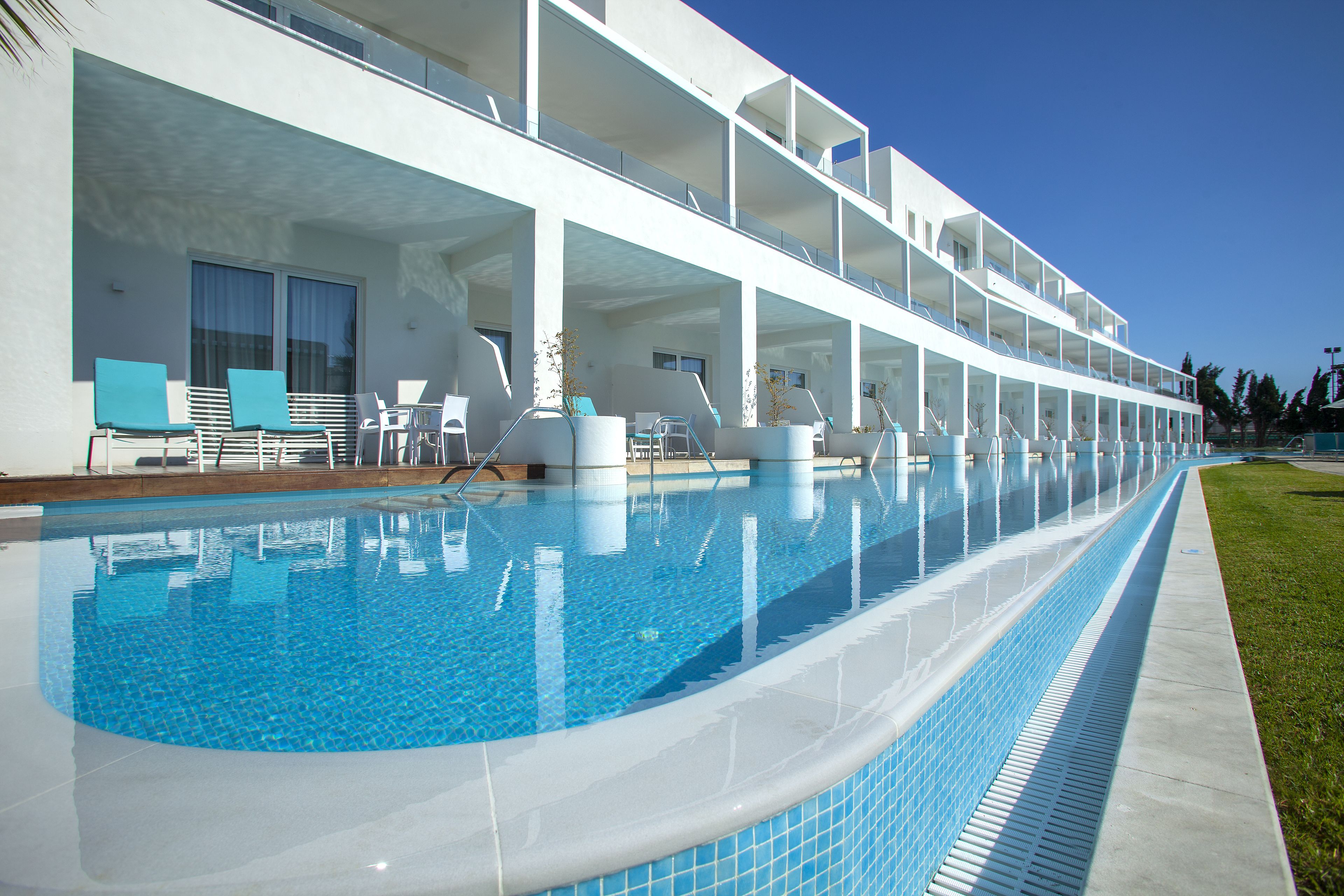 A modern hotel with a long swimming pool, outdoor seating, and a multi-level balcony.
