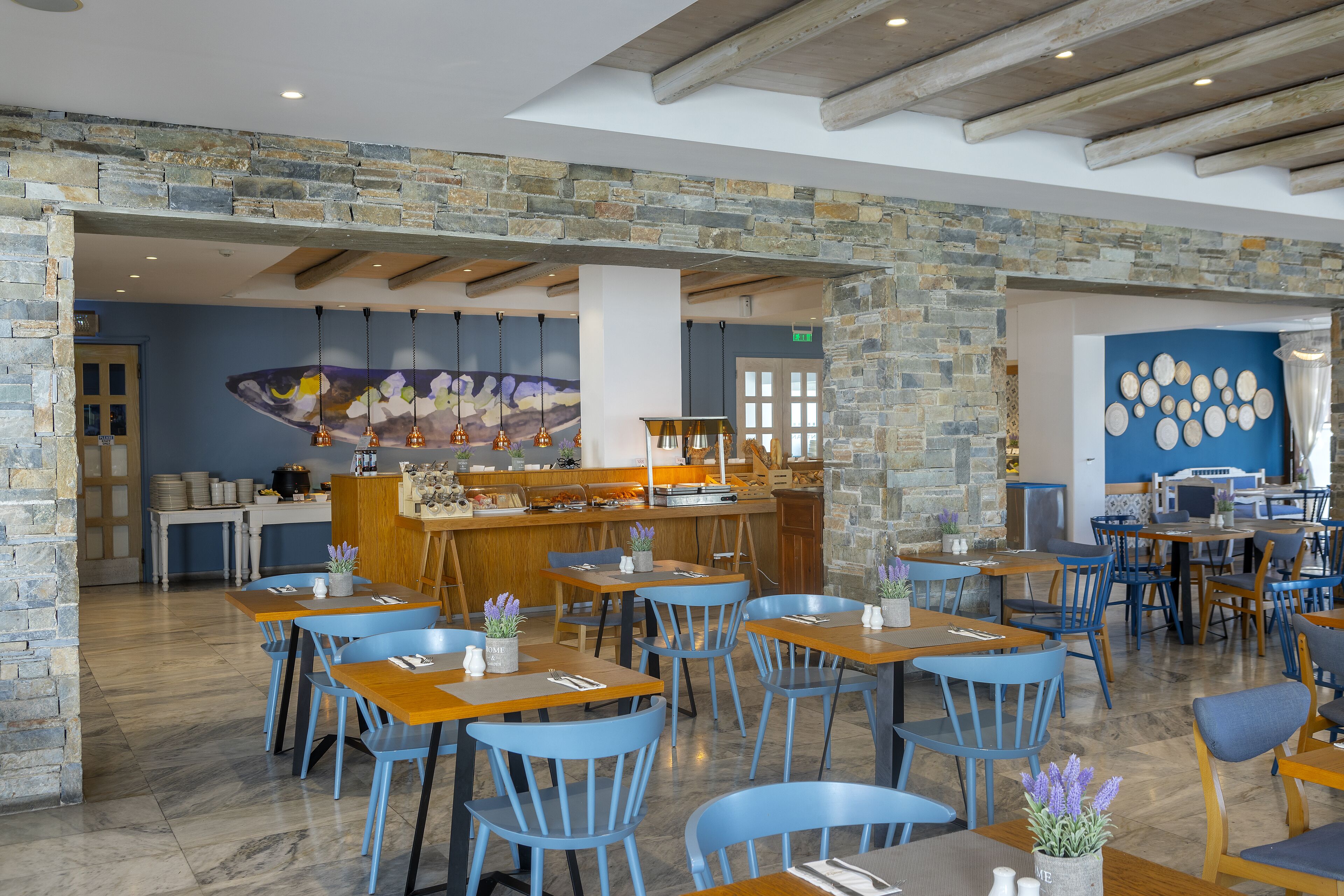 Ein Restaurant mit Stehwänden, Holztischen und blauen Stühlen.