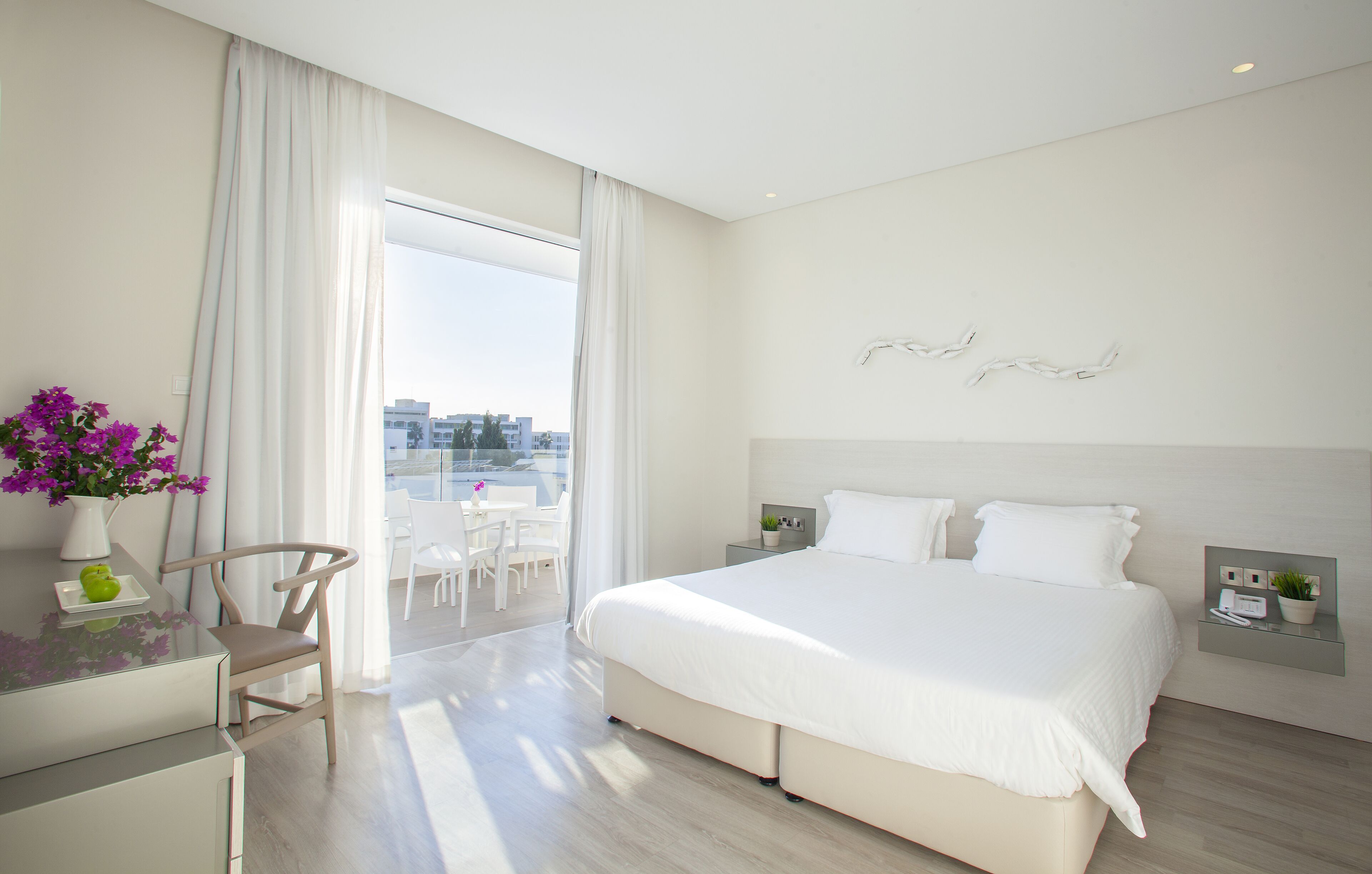 A modern hotel room with a large bed, a desk, and a view of the city through the window.