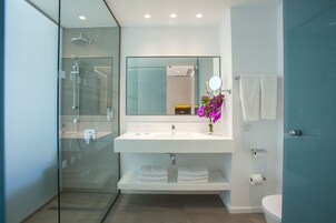 Un baño moderno con ducha de vidrio, lavamanos blanco y espejo sobre él.