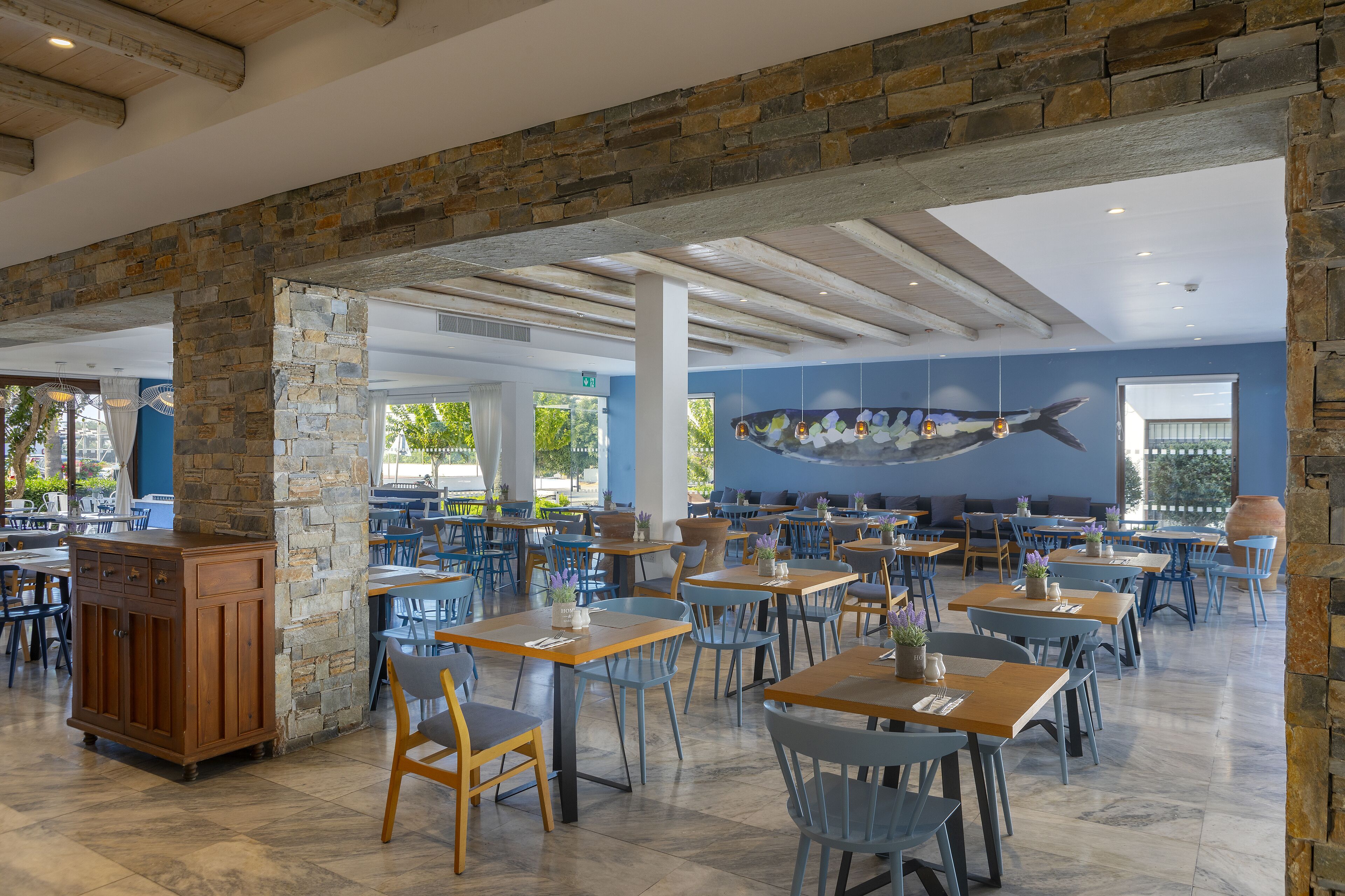 A spacious dining area with stone pillars, blue chairs, and wooden tables.