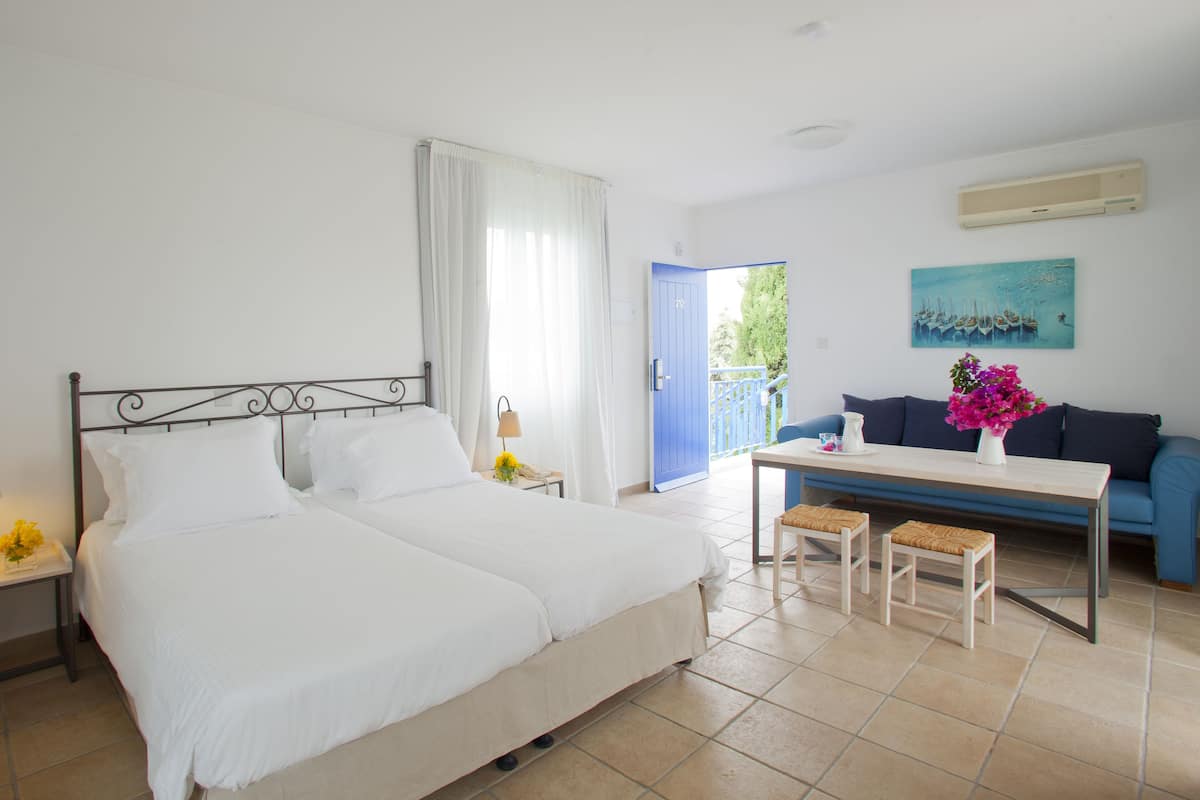 Habitación de hotel con cama doble, mesita de noche con lámpara, una pequeña mesa con un jarrón de flores, un sofá azul y un cuadro en la pared.