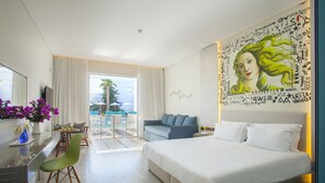 A modern hotel room with a large bed, a desk with a chair, a sofa, and a balcony with a view. - Aliathon Aegean (Geroskipou)