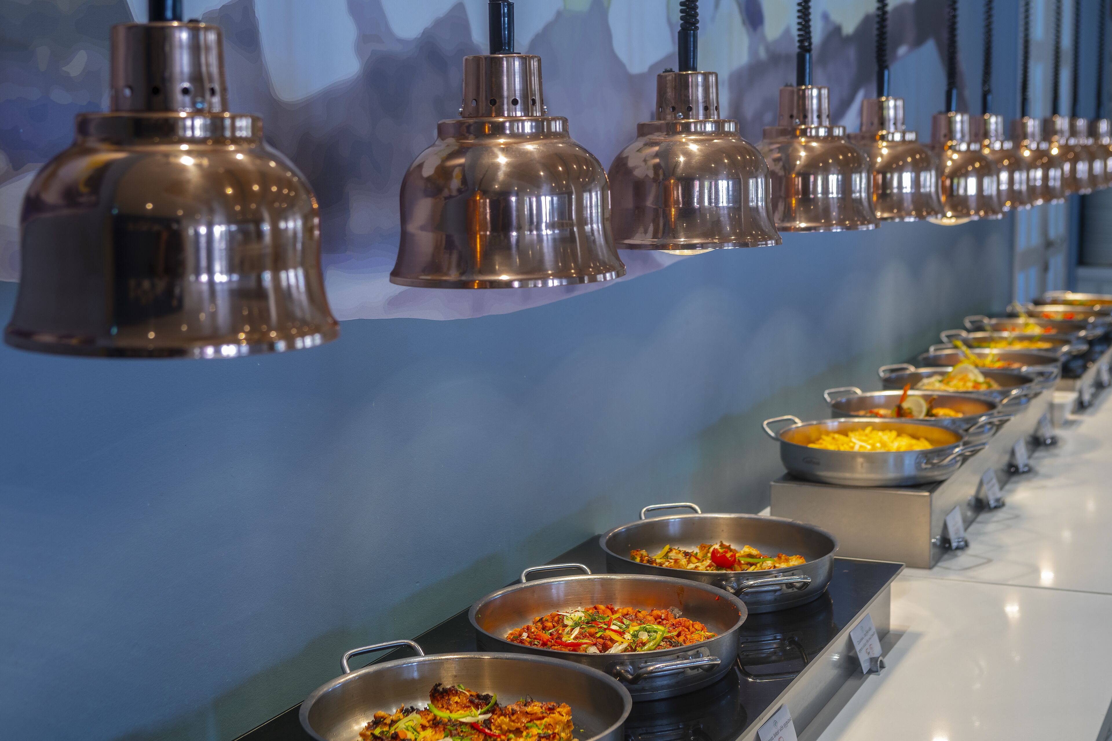 A buffet with various dishes and hanging pendant lights.