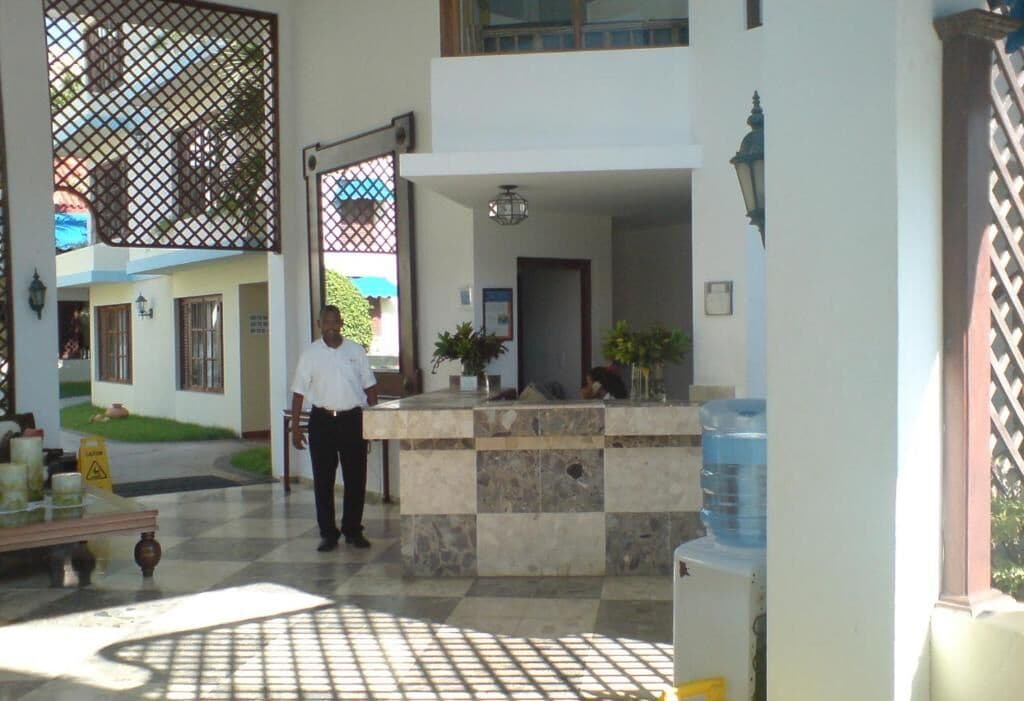 A hotel reception area with a check-in counter, a water dispenser, and a security guard.