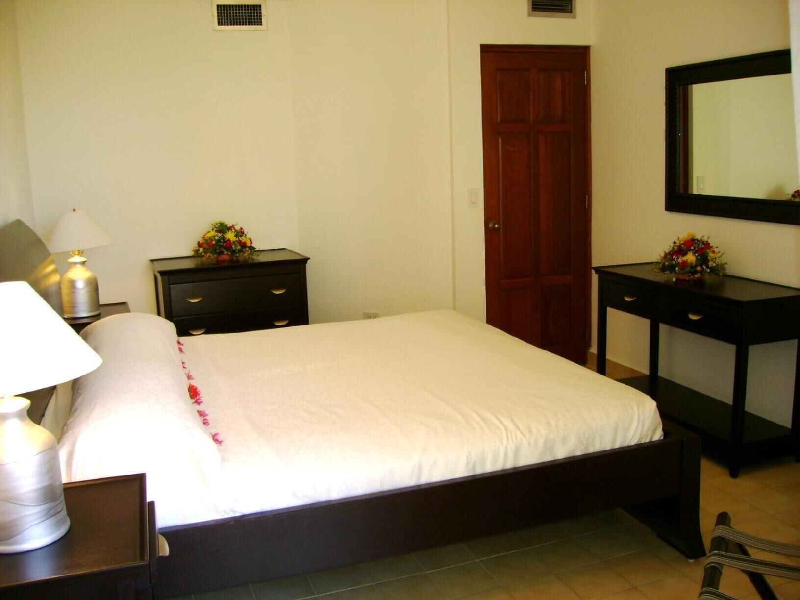 A bedroom with a bed, a nightstand, a dresser, a mirror, and a door.