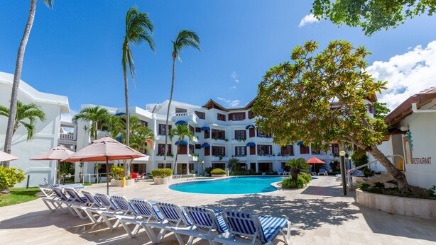 Un resort con piscina, sillas de descanso, palmeras y un restaurante.
