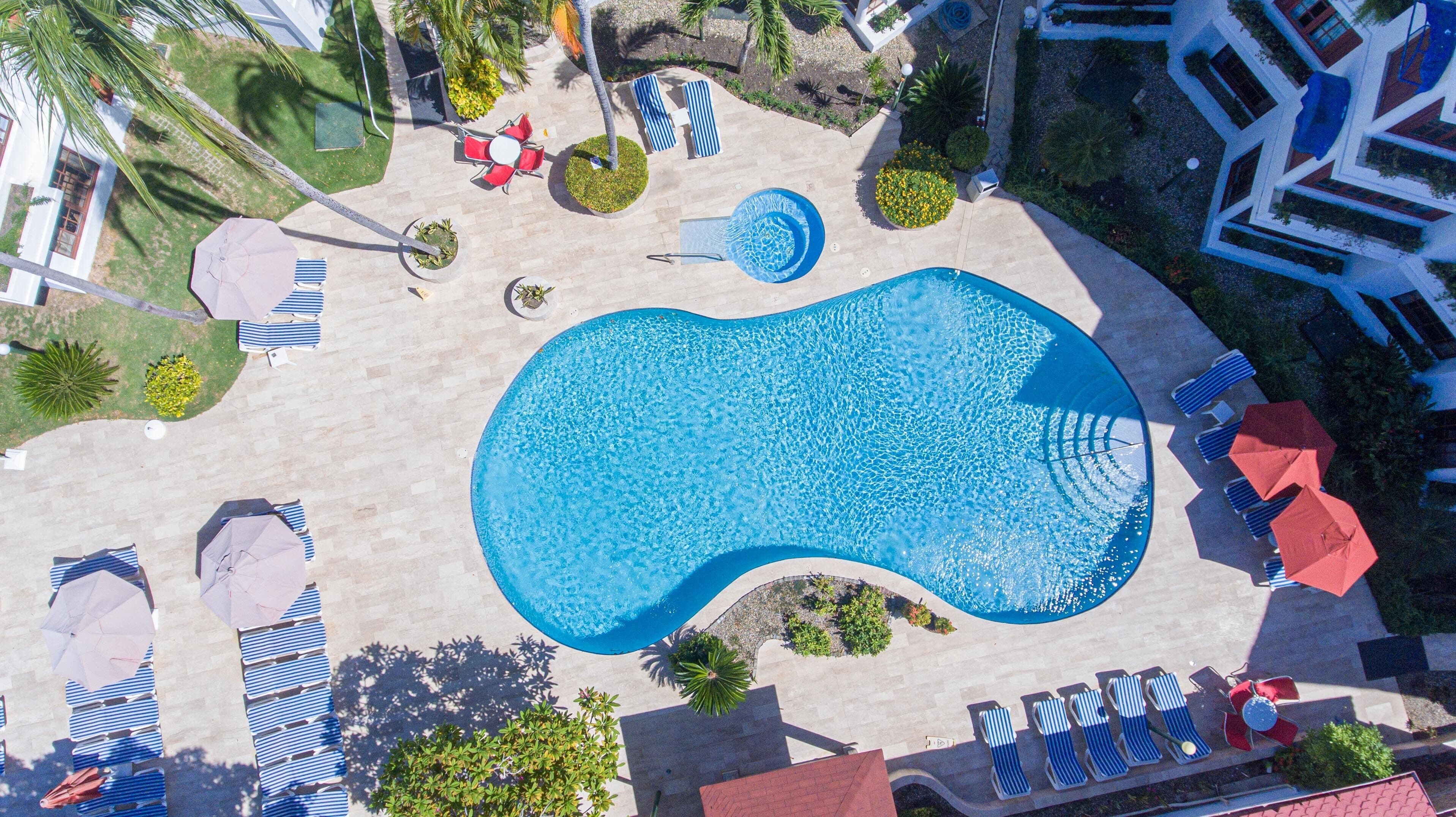 An aerial view of a pool area with lounge chairs, umbrellas, and a central pool.