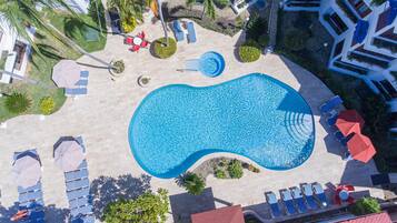 Vista aérea de un área de piscina con sillas de descanso, sombrillas y una piscina central.