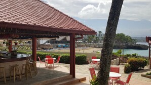 Un área de estar al aire libre con vista a la piscina, que incluye un porche cubierto, sillas rojas y blancas, y una zona de bar.