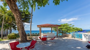 Un patio al aire libre con sillas rojas y una mesa, con vistas a una piscina y al mar.