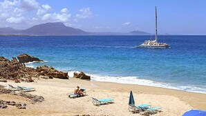 Una playa con un velero, costa rocosa y sillas de playa.
