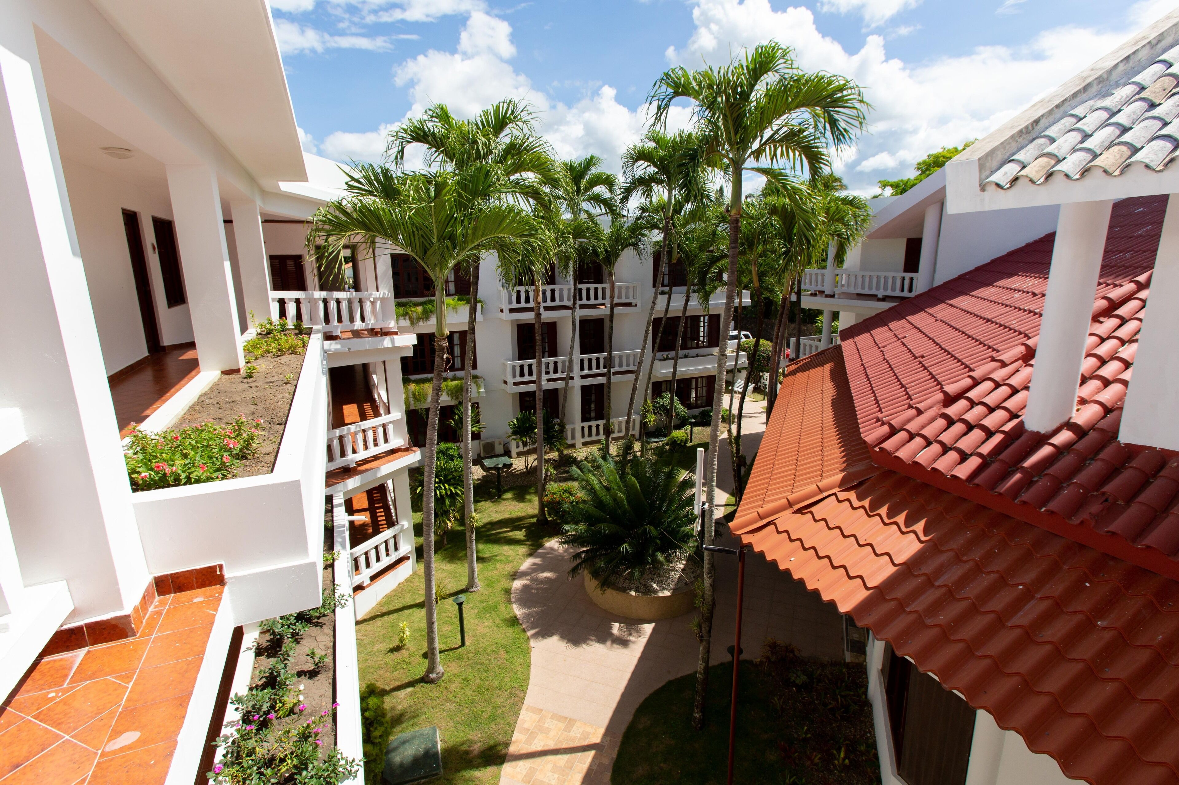 Un patio de hotel con varios balcones, palmeras y un tejado de baldosas.