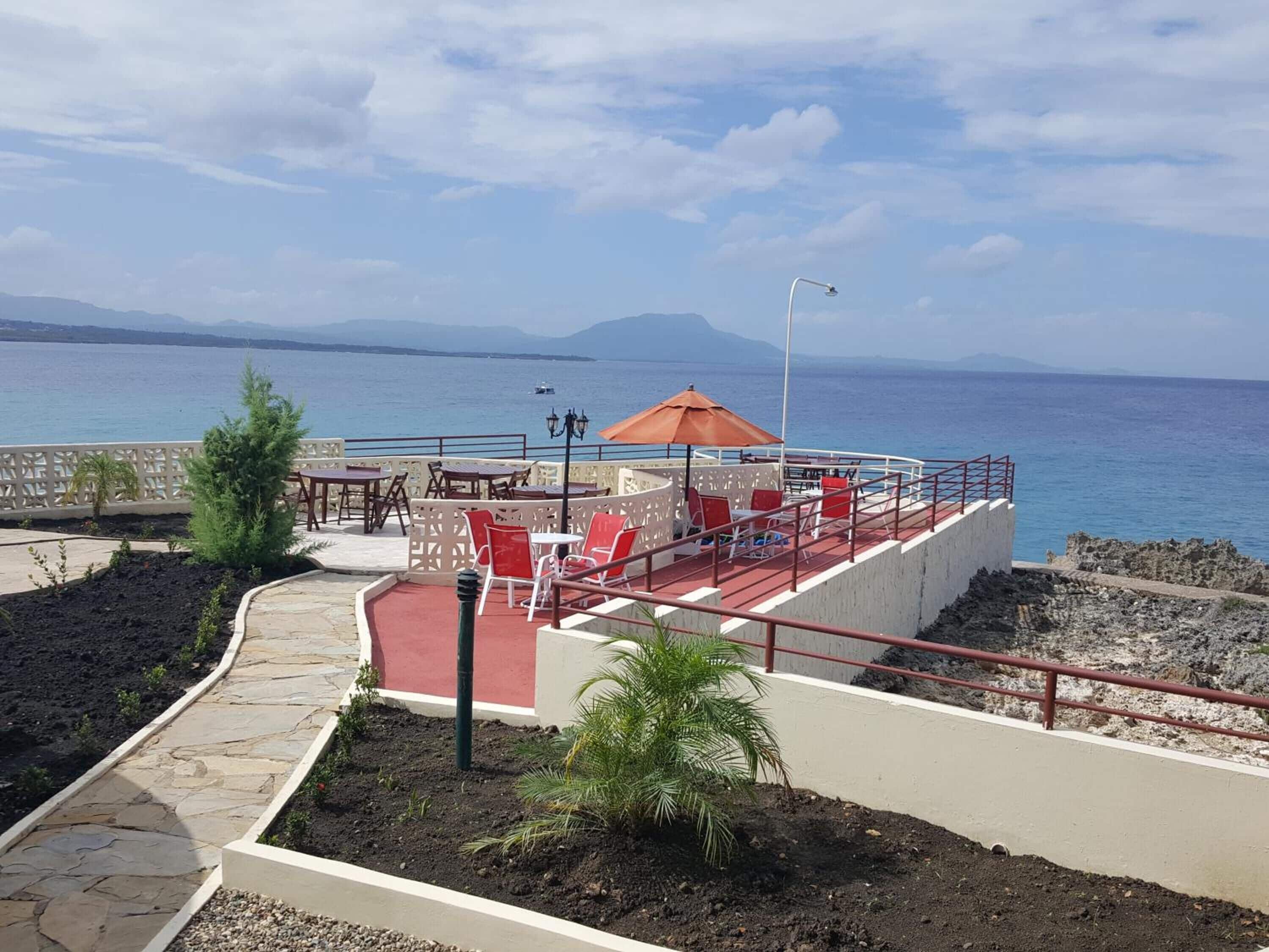 Una terraza con mobiliario exterior, vista al mar y montañas al fondo.