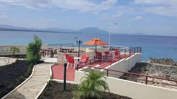 Una terraza con mobiliario exterior, vista al mar y montañas al fondo.