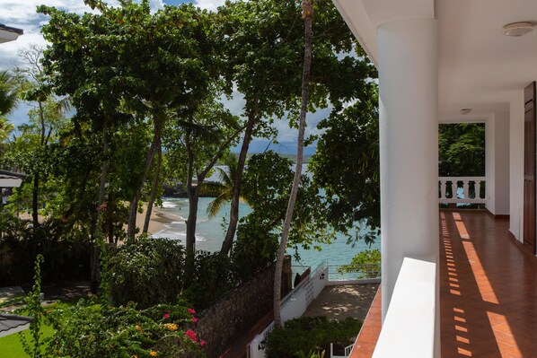 A balcony with a view of the sea and lush greenery.