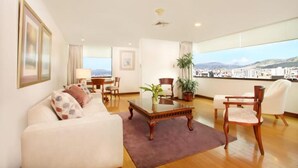 Amplia sala de estar con un gran ventanal que ofrece vistas de la ciudad, un sofá cómodo, una mesa de centro de madera y un comedor con sillas.