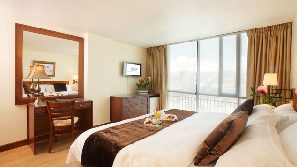 A hotel room with a bed, a desk, a chair, a television, and a window with curtains. - Rio Amazonas Hotel (Quito)
