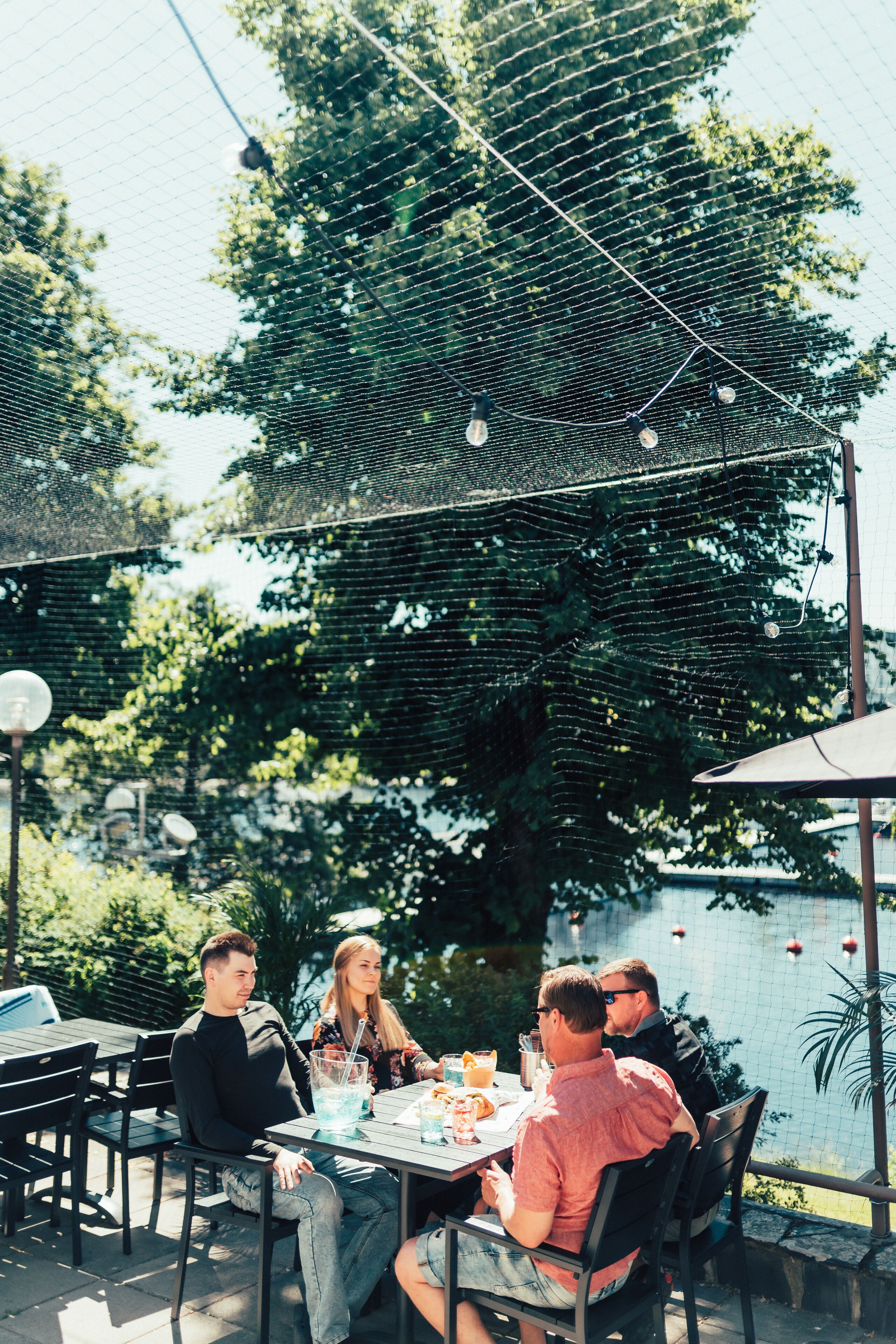 An outdoor dining area with a table and chairs, surrounded by a wire mesh fence and trees.