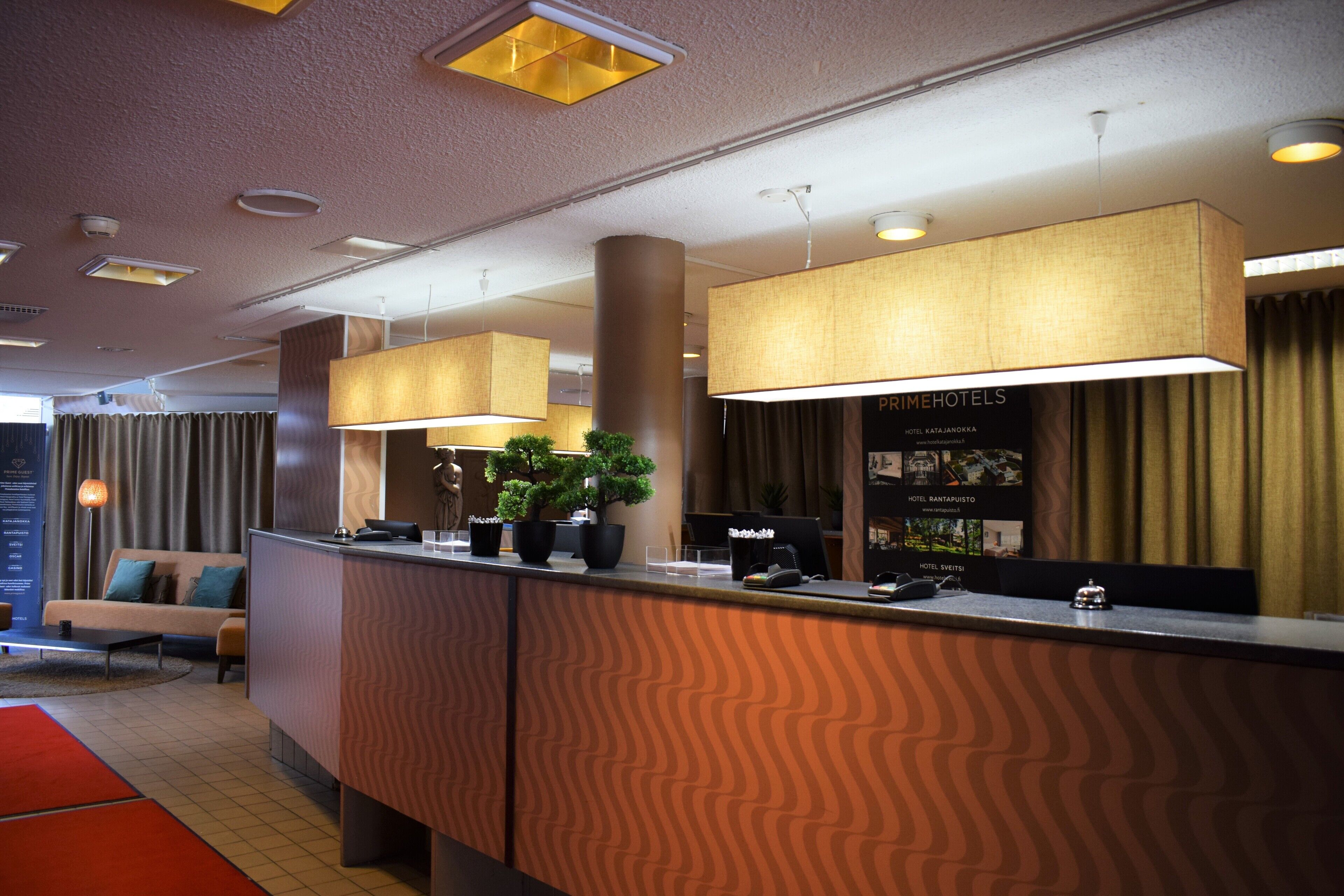 A hotel reception area with a modern design, featuring a reception desk, potted plants, and a large sign displaying hotel names.
