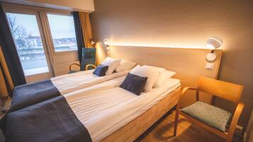 A double bed with two pillows, a bedside table with a lamp, and a chair with a cushion.