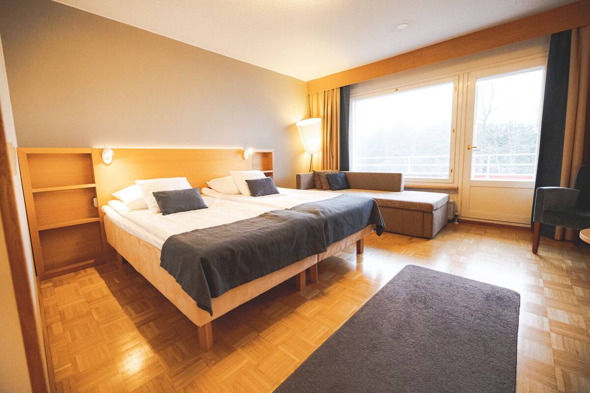 A hotel room with a large bed, a desk, and a window with curtains.