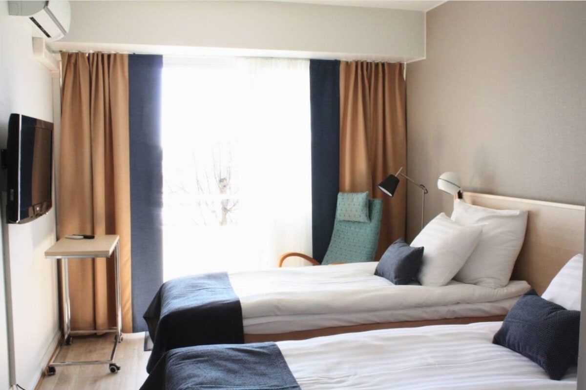 Habitación de hotel con dos camas, televisor, escritorio y ventana con cortinas.
