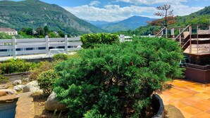 A terrace with a view of mountains, a white fence, and a wooden deck. - Hotel Christina Lourdes (Lourdes)