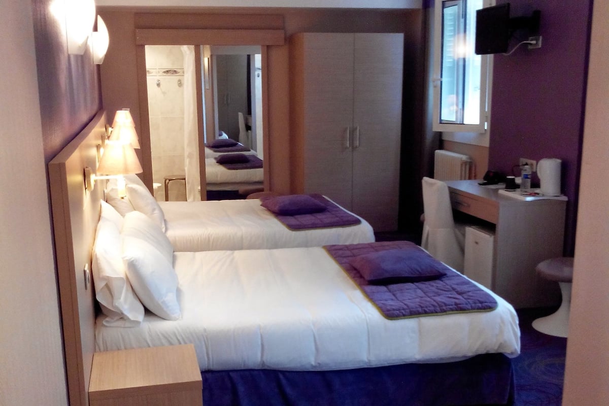 Habitació d'hotel amb dos llits, una taula de nit, una cadira, un mirall i una finestra.