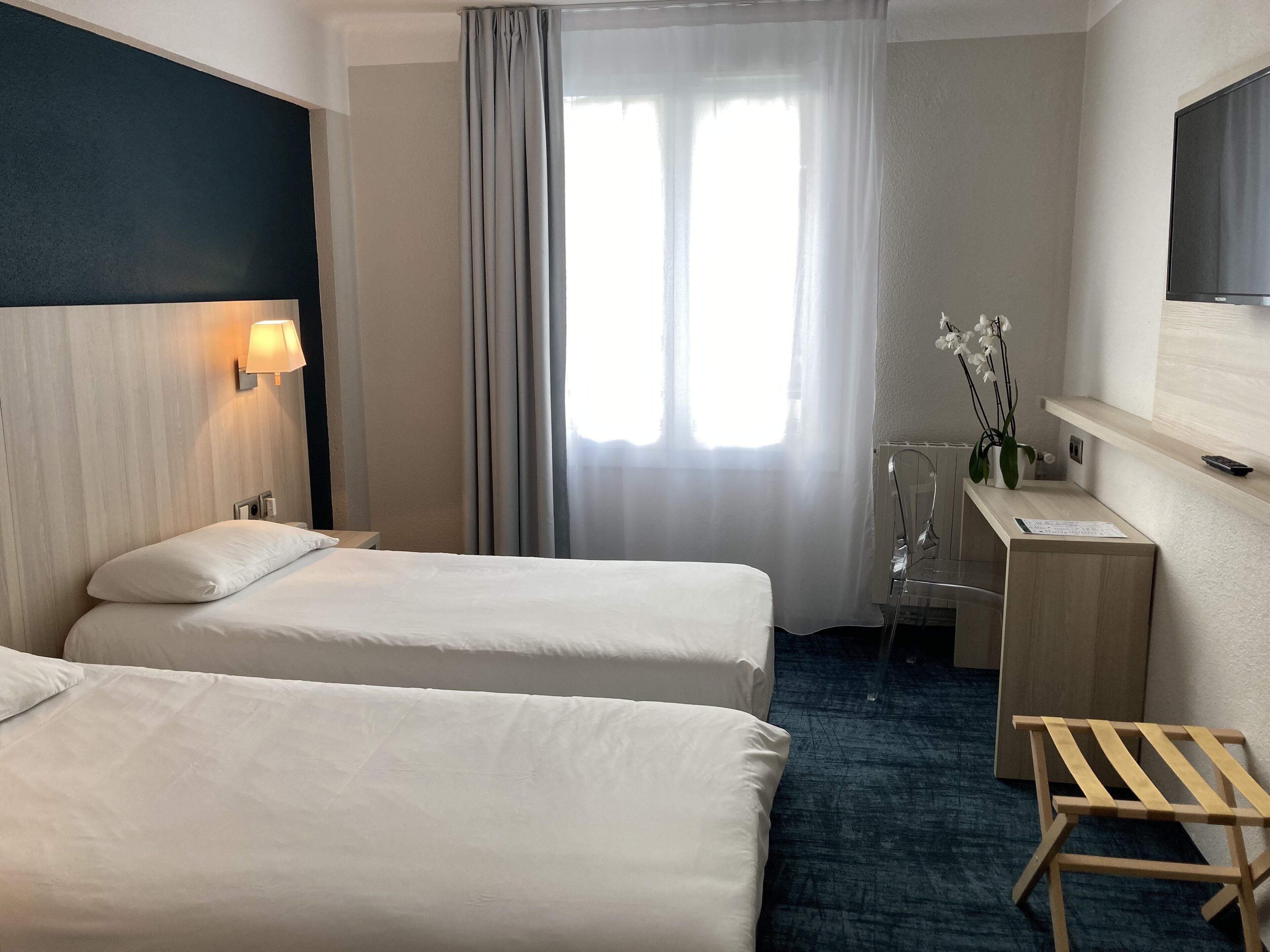 A hotel room with two beds, a desk, a chair, a TV, and a window with curtains.