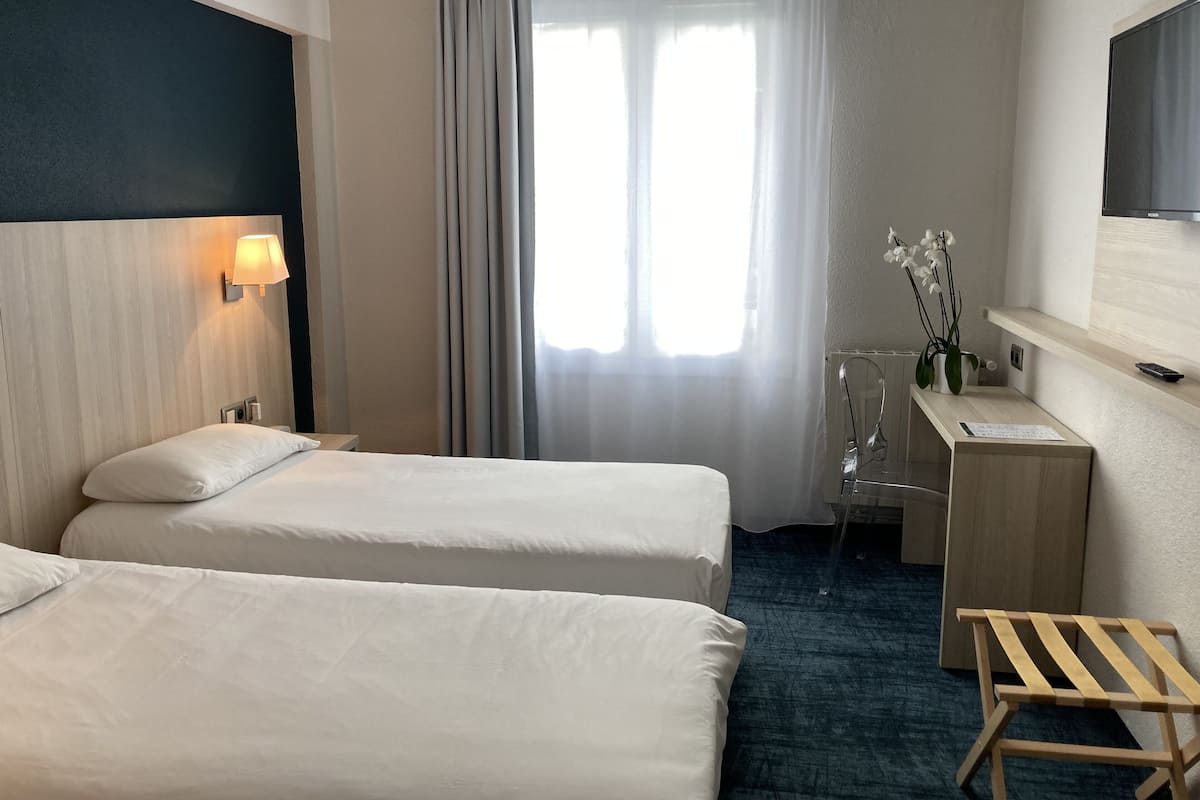 Habitació d'hotel amb dos llits, escriptori, cadira, televisió i finestra amb cortines.