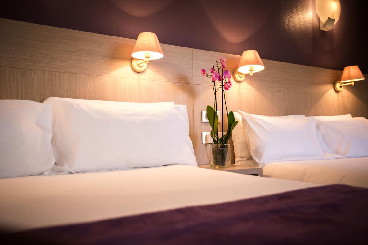 Habitació d'hotel amb dos llits, cada un amb roba de llit blanca, una tauleta de nit amb una orquídia en maceta i làmpades penjades a la paret.